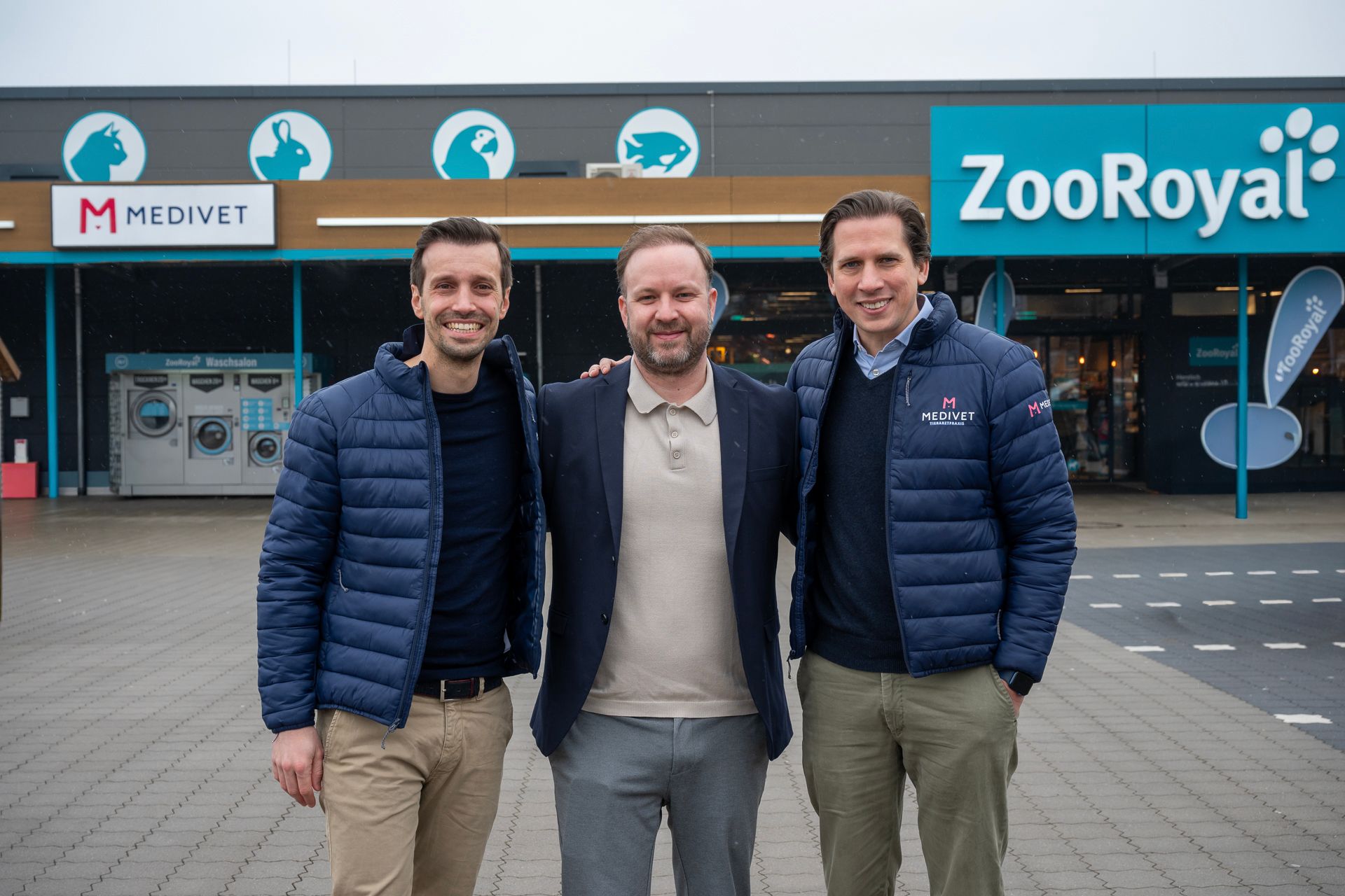 Drei Männer stehen vor einem Tierbedarfsgeschäft. Einer trägt ein Sakko, zwei blaue Jacken.