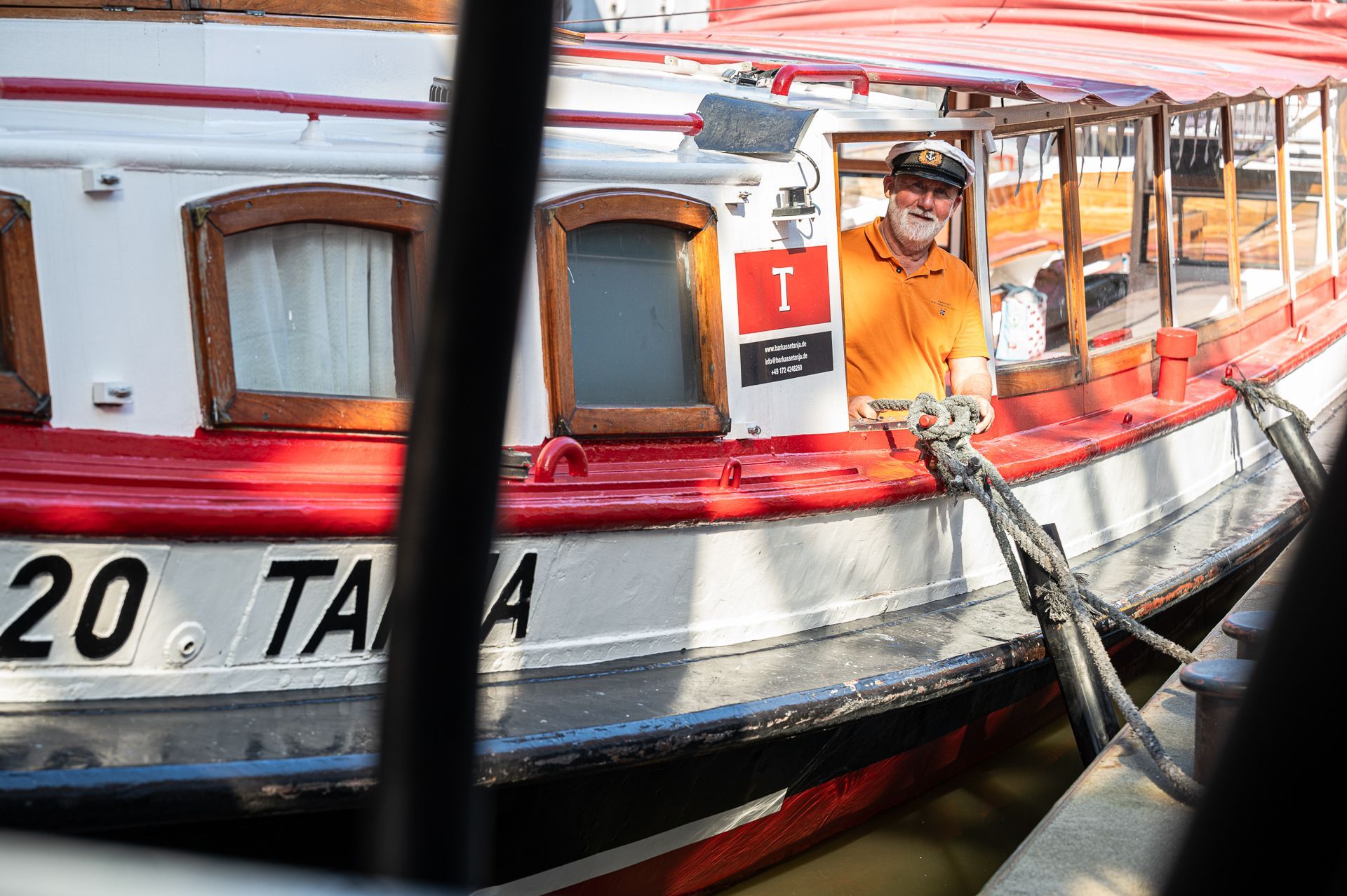 Mann in orangefarbenem Hemd auf einem rot-weißen Boot namens „TARA“ befestigt ein Seil.