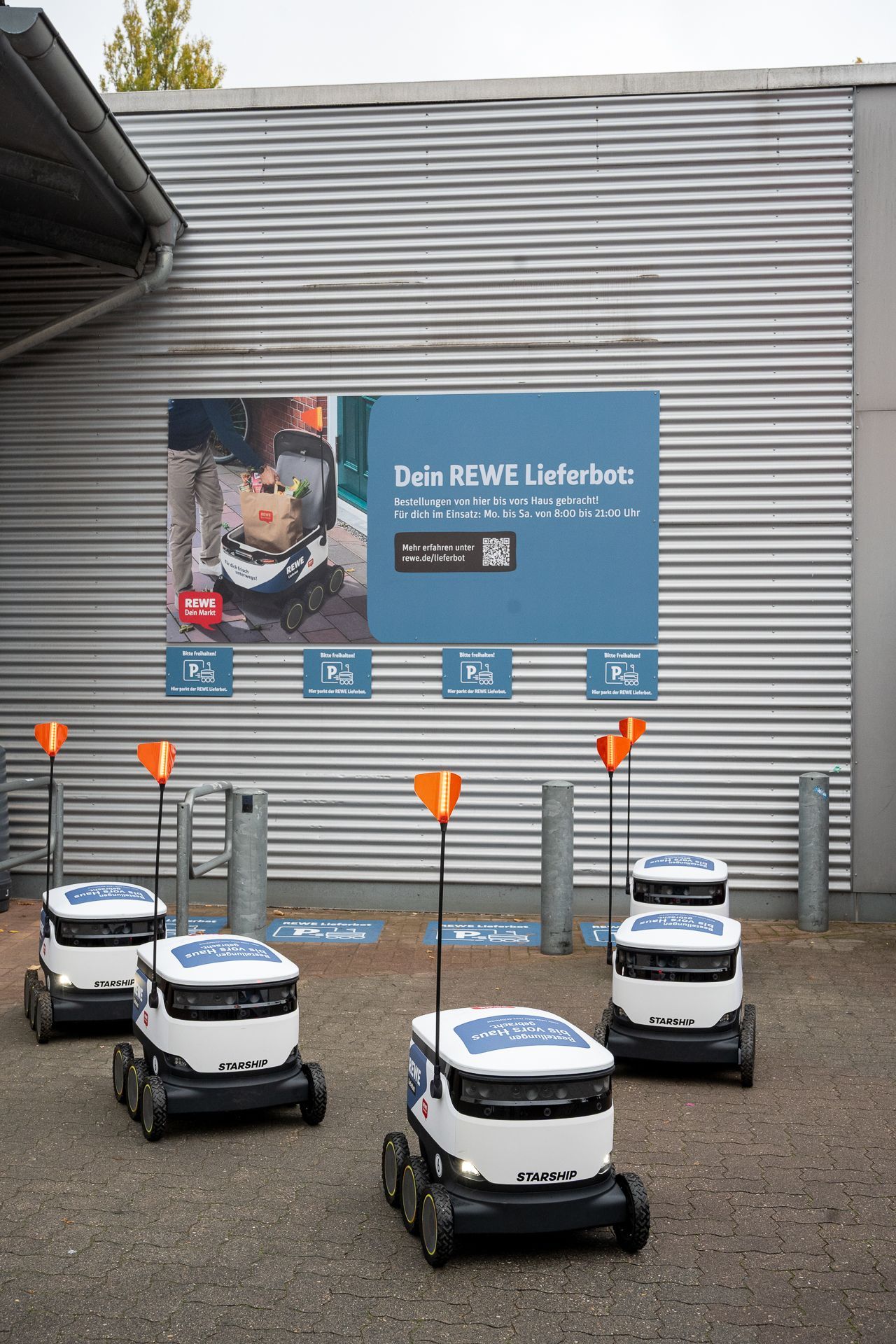 Roboter parken in der Nähe eines Gebäudes mit einem Schild und orangefarbenen Fahnen.