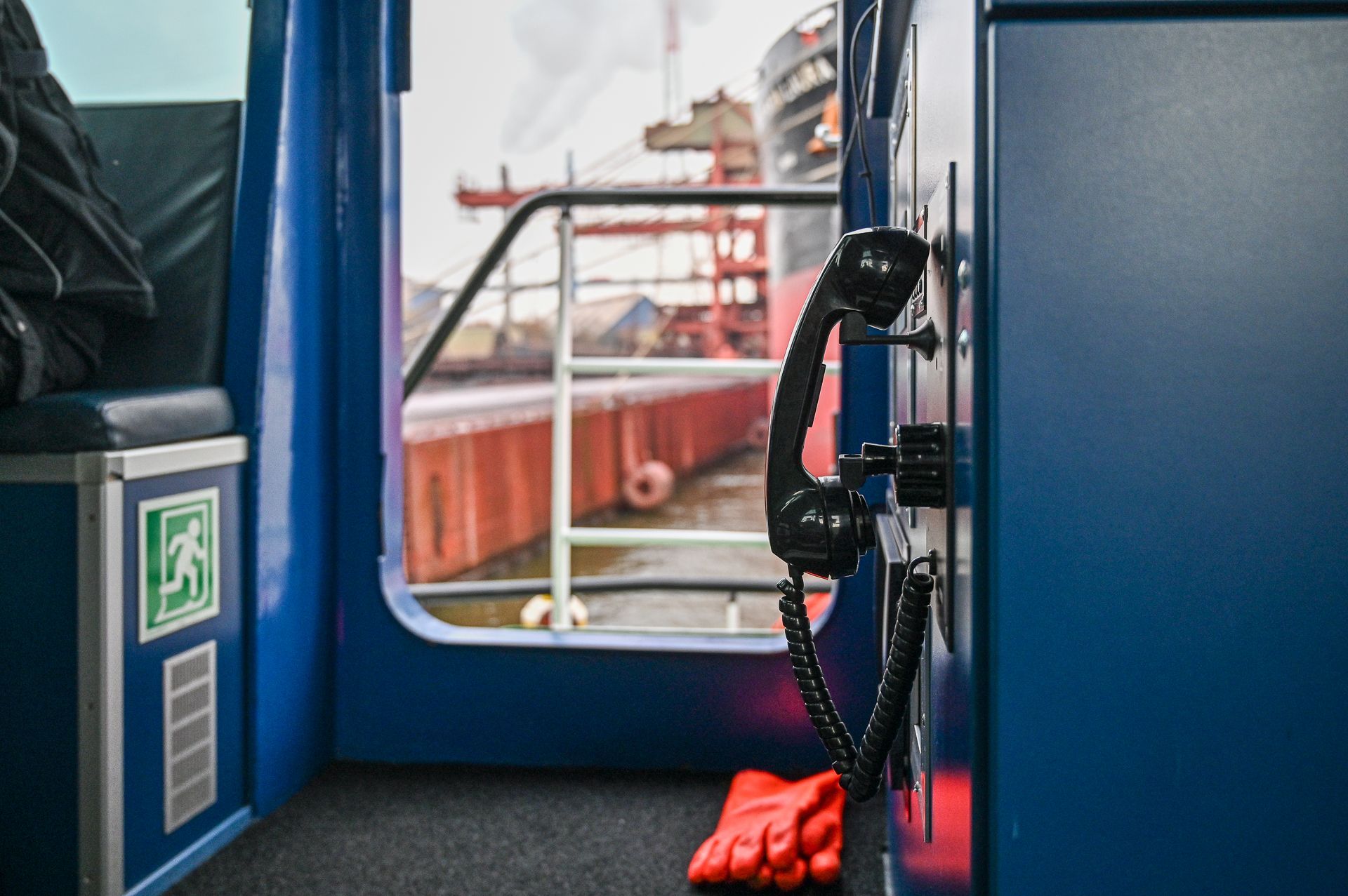 Innenansicht einer blauen Kabine auf einem Schiff mit einem schwarzen Telefon, einer offenen Tür und einem roten Handschuh.
