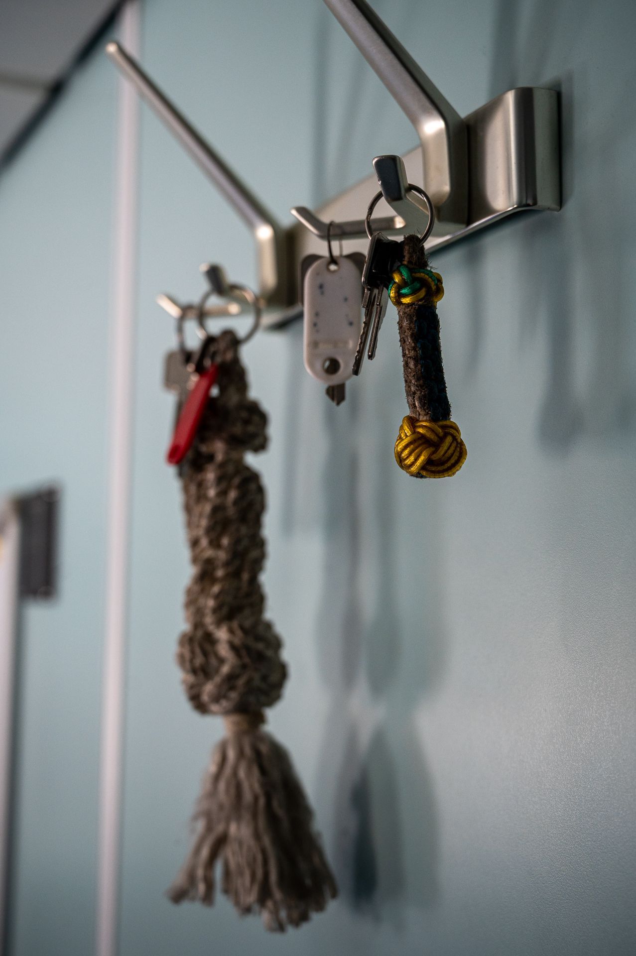 Schlüssel hängen an einem silbernen Wandhaken vor einer hellblauen Wand.