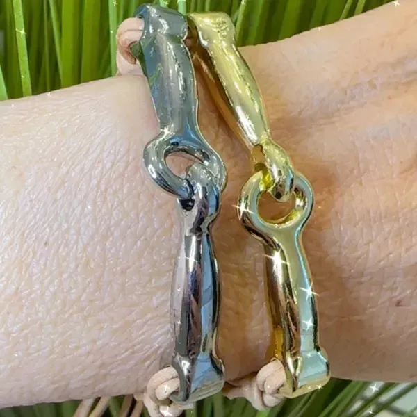Two metallic bracelets, one silver and one gold, on a wrist against a green background