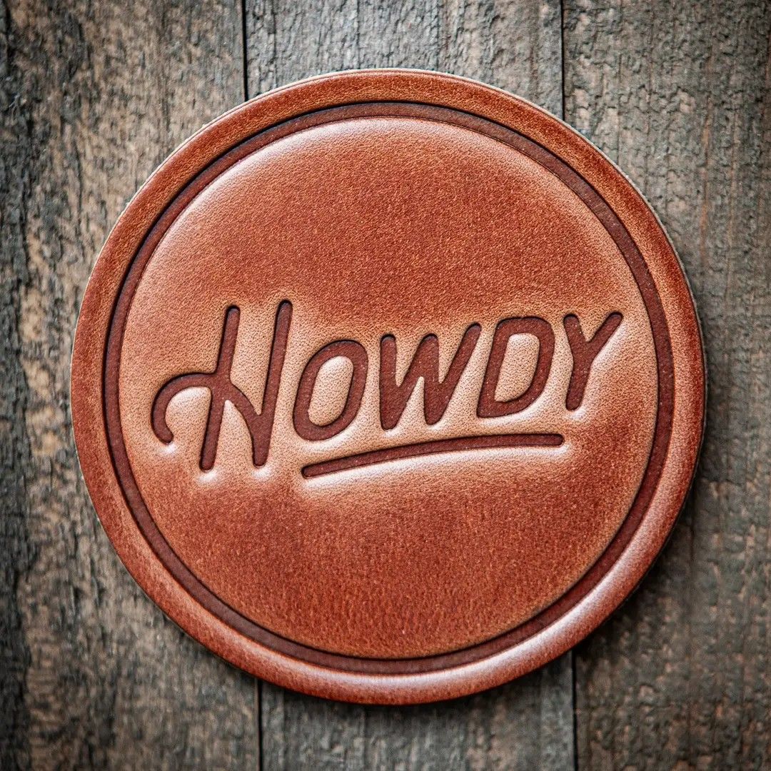 Rustic round brown badge with raised “Howdy” lettering on a weathered wood background