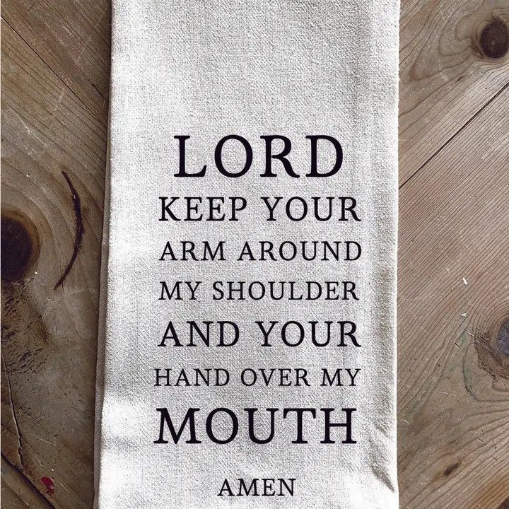 White cloth towel with black religious quote: “Lord keep your arm around my shoulder and your hand over my mouth. Amen.”