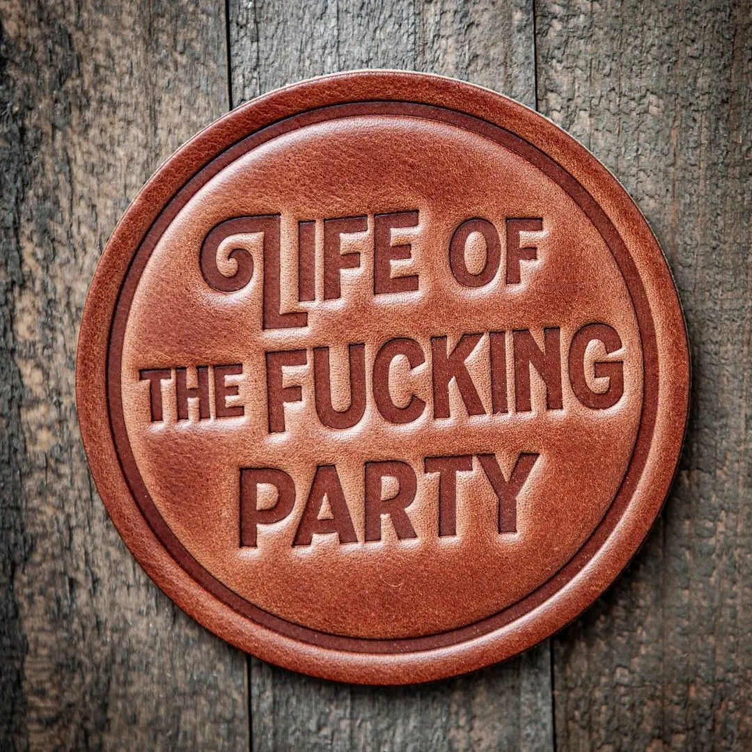 A round brown button on weathered wood reads “Life of the Fucking Party.”