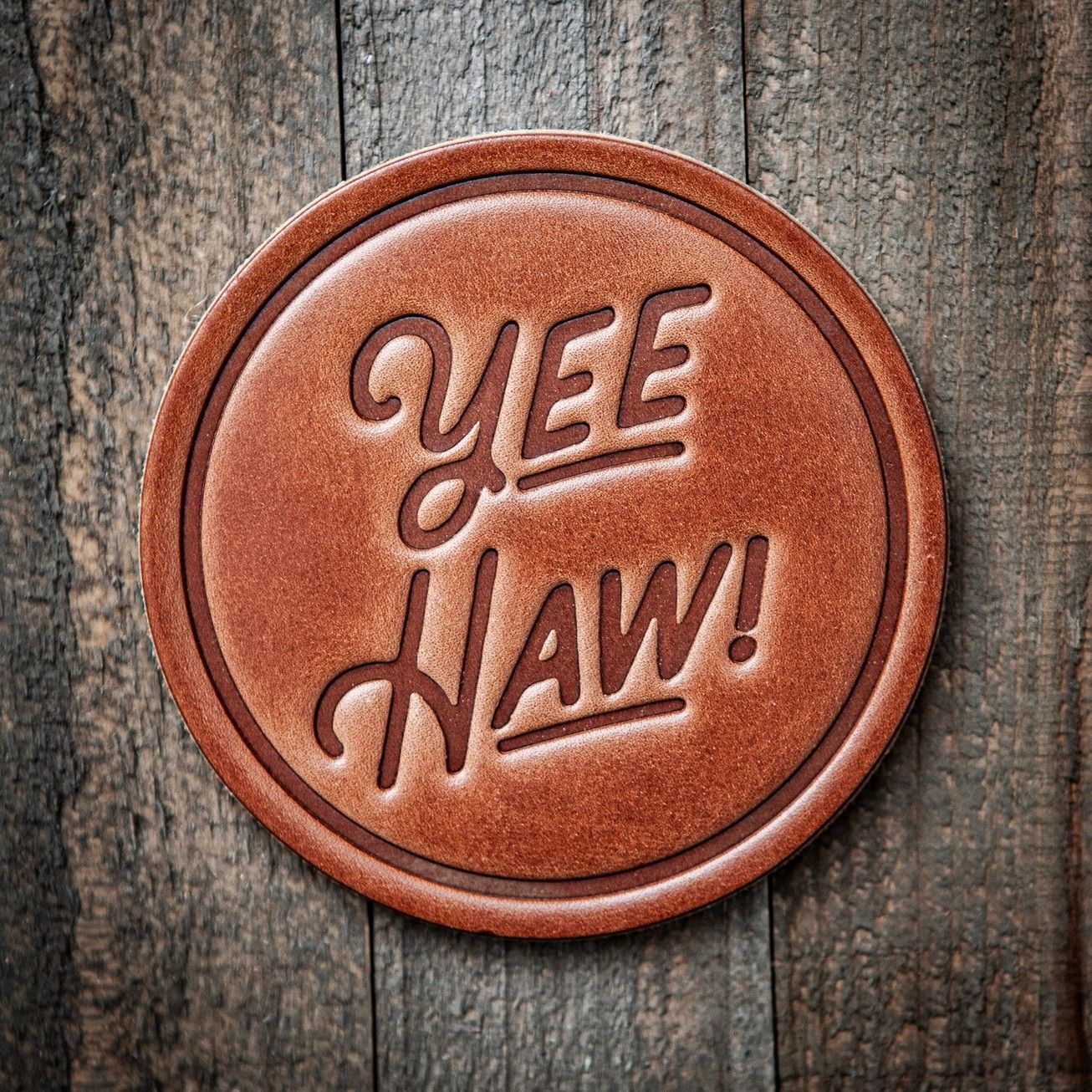 Round leather coaster embossed with “Yee Haw!” on a rustic wood background