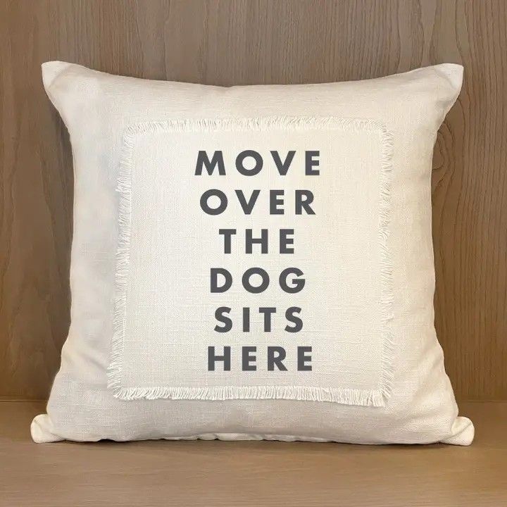 White pillow with bold black text: “MOVE OVER THE DOG SITS HERE.”