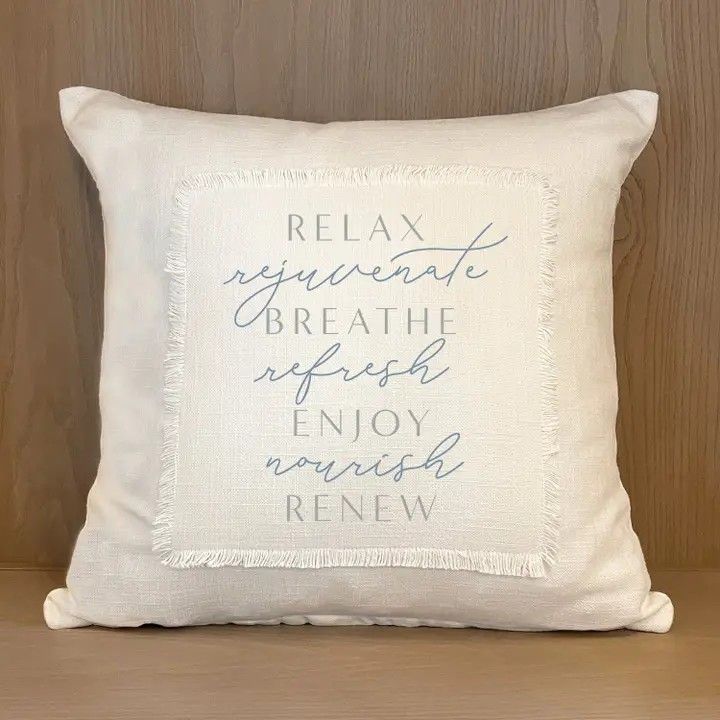 Cream throw pillow with “Relax, rejuvenate, breathe, refresh, enjoy, nourish, renew” text on wooden chair