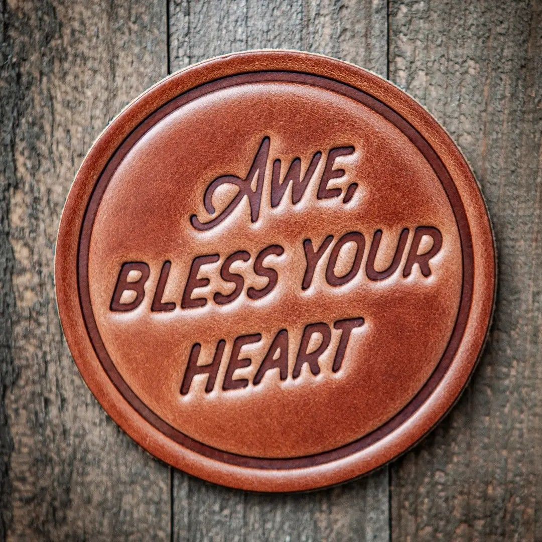 Brown circular plaque on weathered wood reading “Awe, bless your heart”
