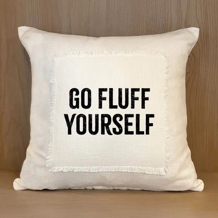 Cream pillow with bold black text reading “GO FLUFF YOURSELF” on a wooden surface.