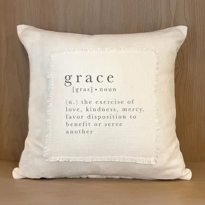 White throw pillow with the word “grace” and a definition printed on it, against a wood background