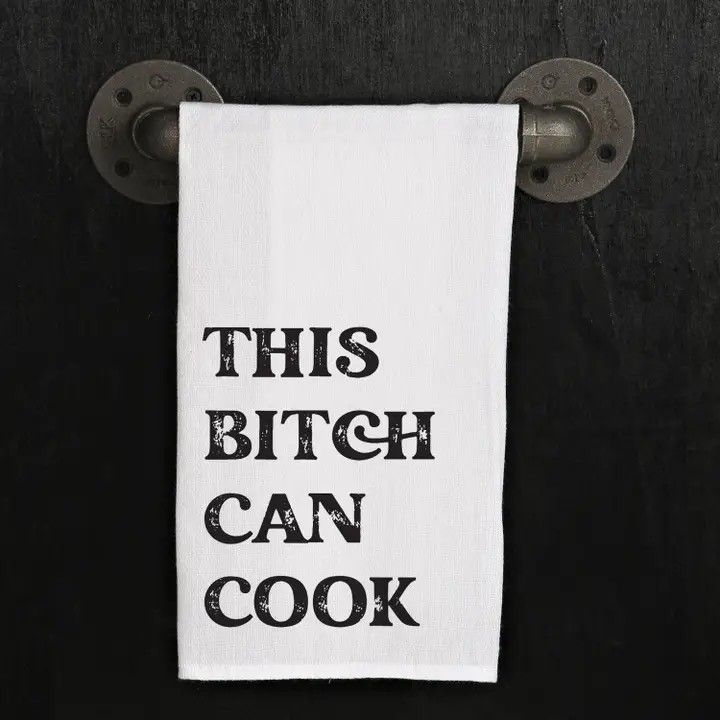 White towel with bold black text hangs on dark wall: “THIS BITCH CAN COOK.”