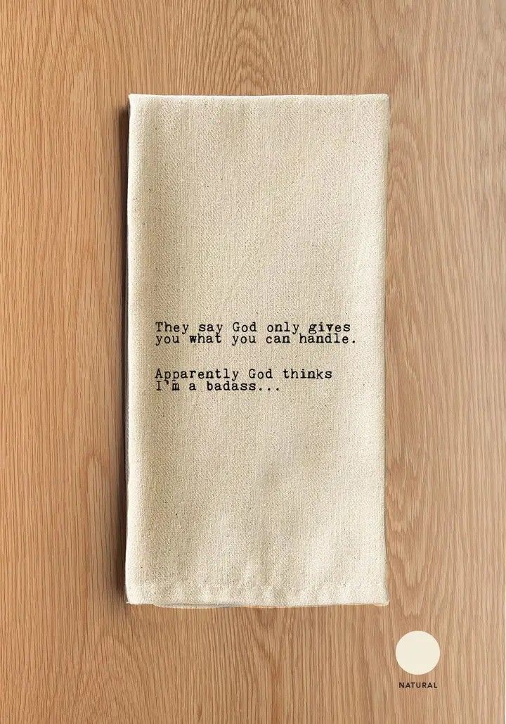 Small beige fabric pouch with black text, lying on a wooden surface.