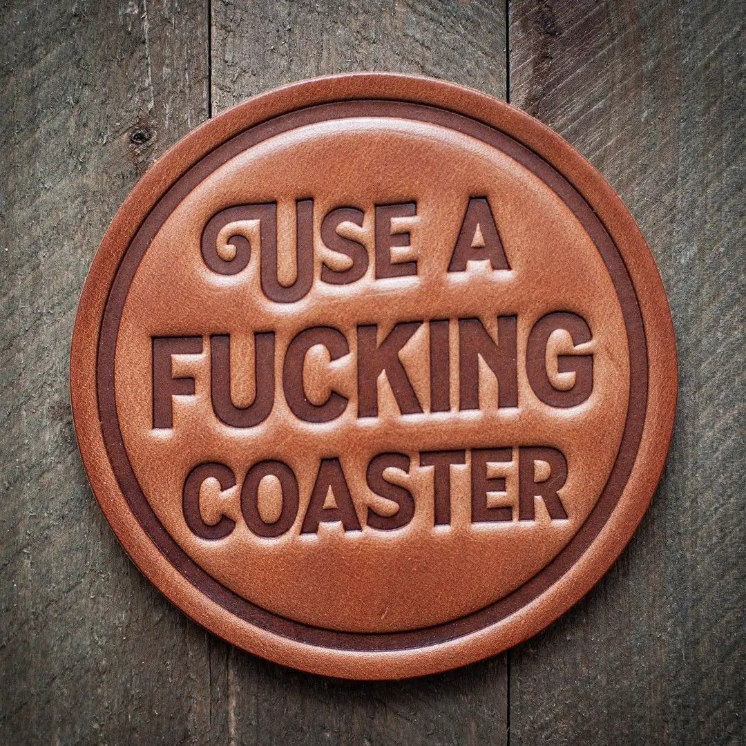 Round wooden coaster with engraved text: “USE A FUCKING COASTER.”