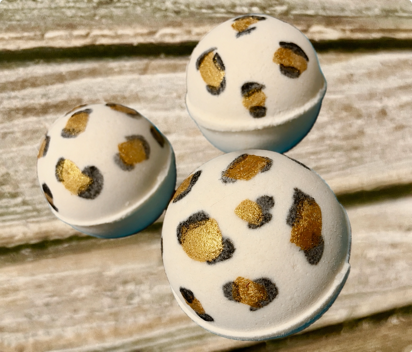 Three white golf balls with gold-and-black leopard spots on a weathered wooden surface.