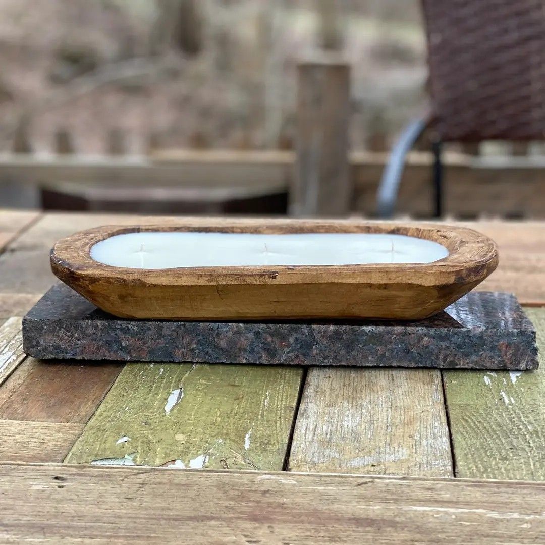 Wooden oval soap dish with white soap on a slate slab atop a weathered table outdoors