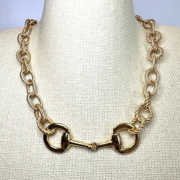 Gold chain necklace with oval links and a central clasp on a beige display bust