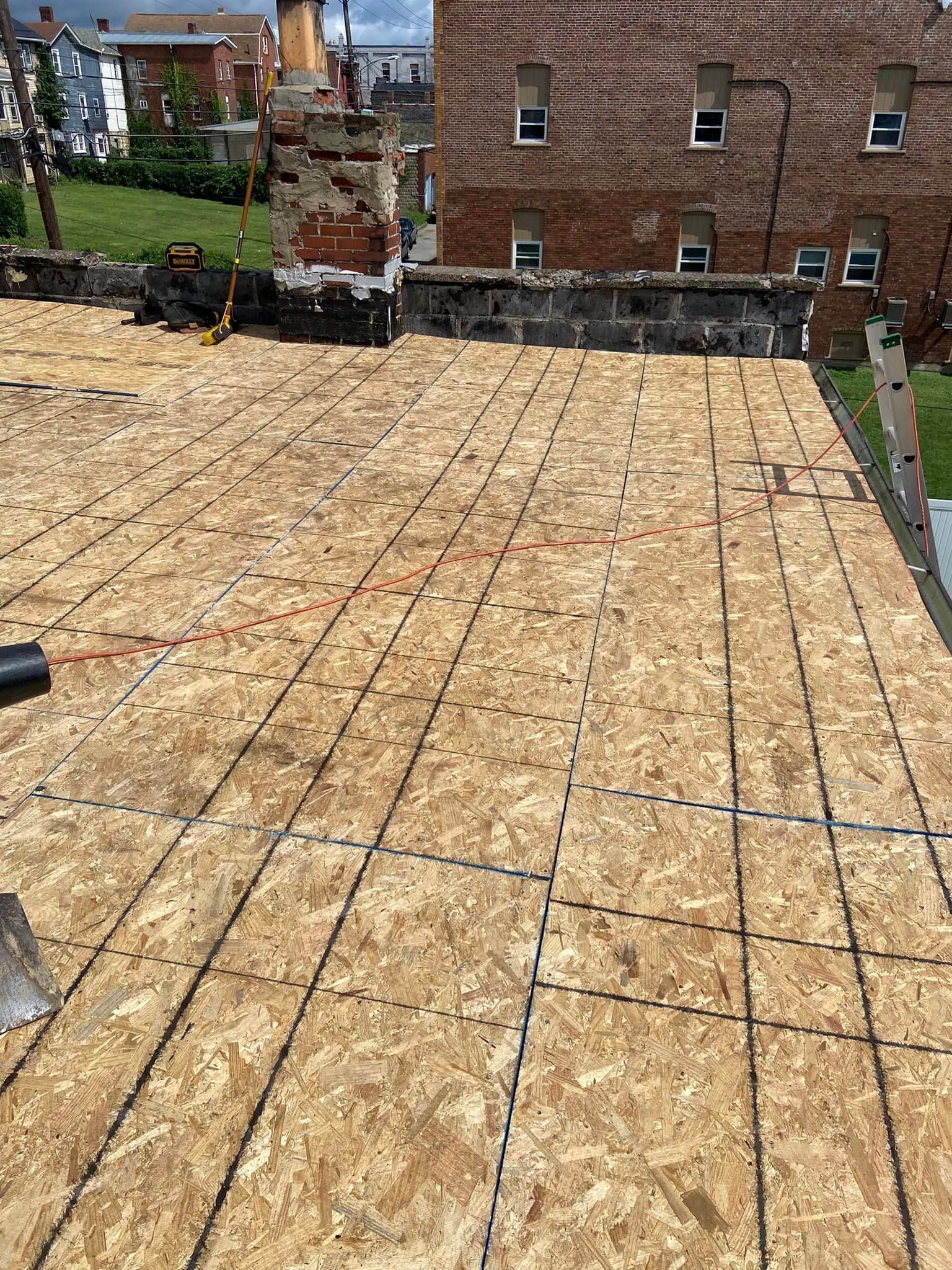 Rooftop with new OSB boards installed, ready for roofing. City buildings in the background.
