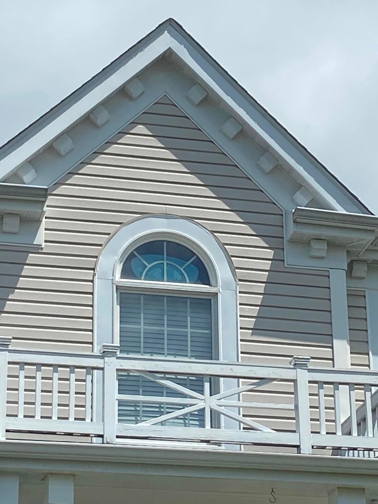 White house facade with arched window, balcony, and beige shingles.