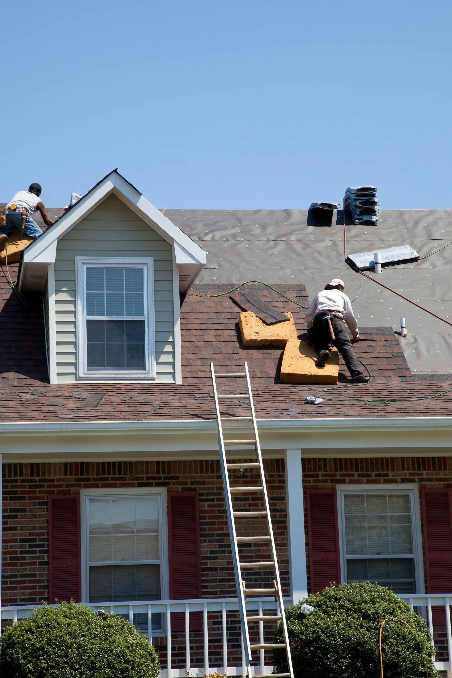 Workers repairing a roof with a ladder leaning against a two-story house