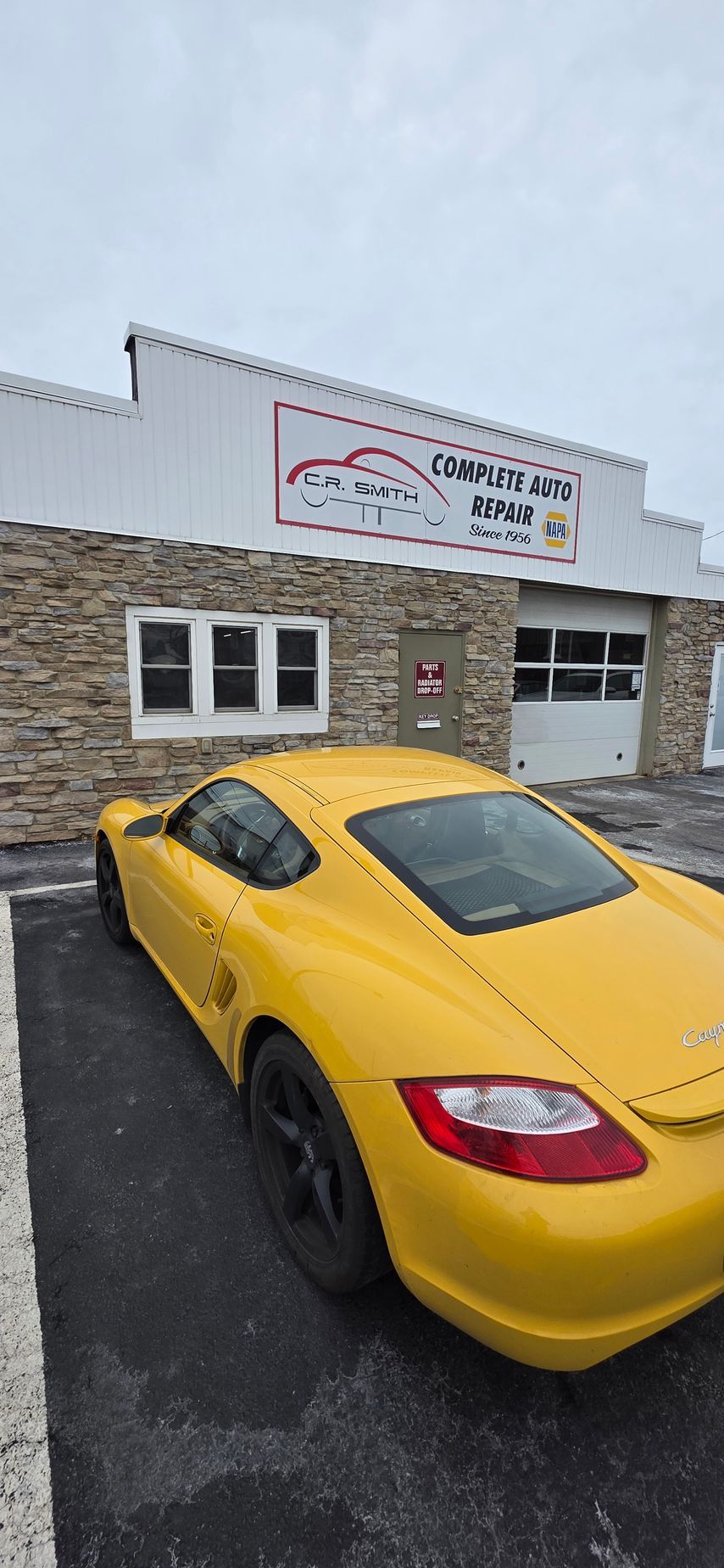 A yellow Porsche parked in front of a stone-faced building with a sign that reads 
