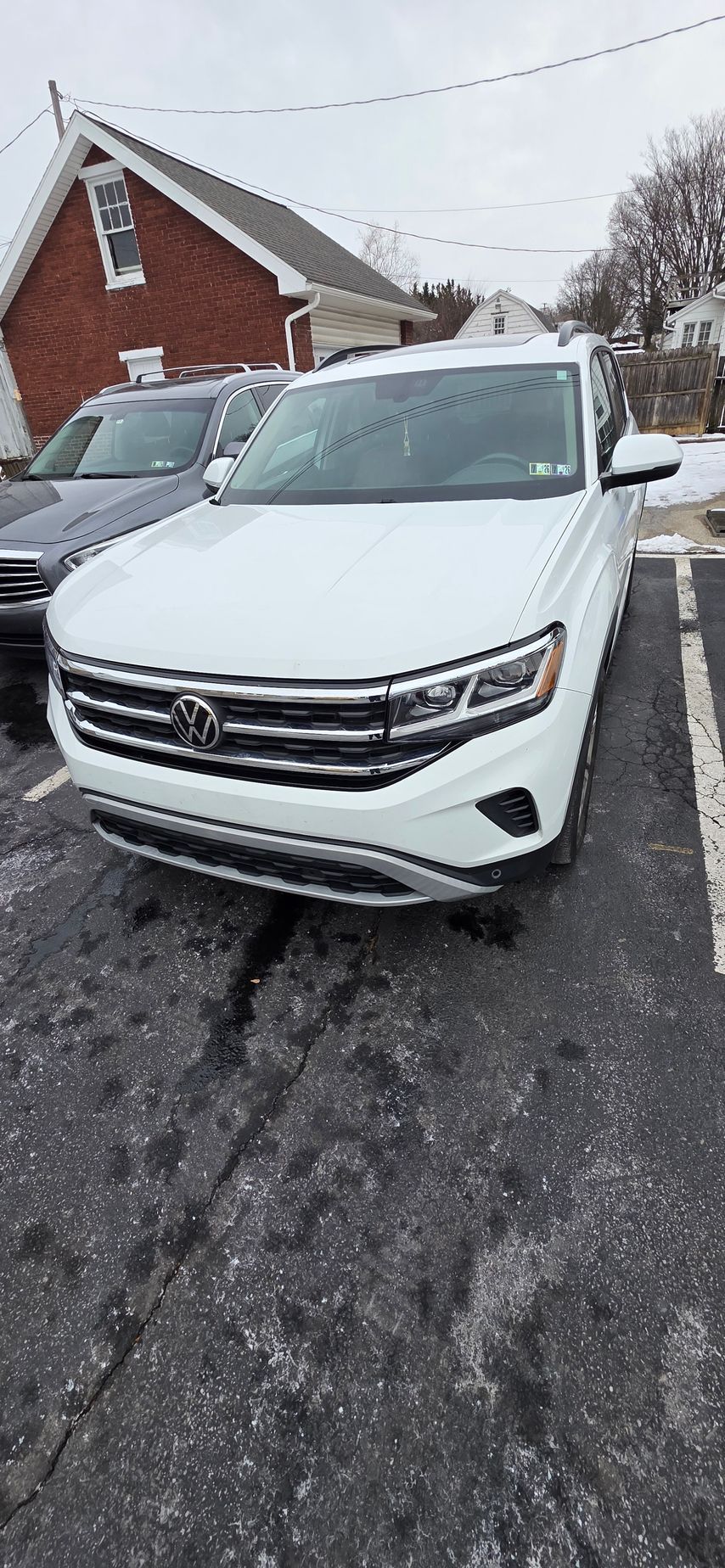A white Volkswagen SUV parked in a paved lot in front of a red brick building during a winter day.