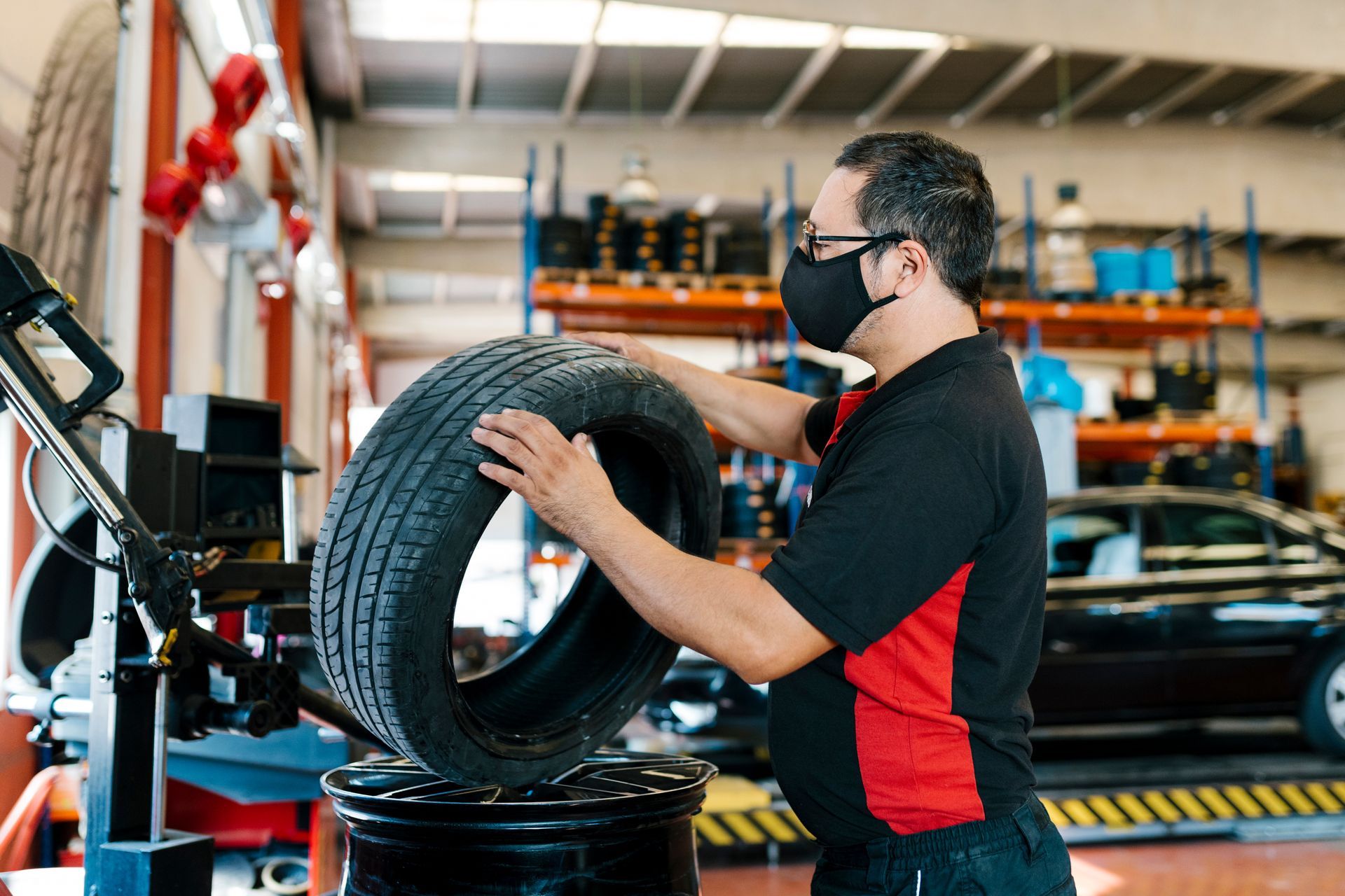 A mechanic wearing a mask is examining a tire in an auto repair shop.