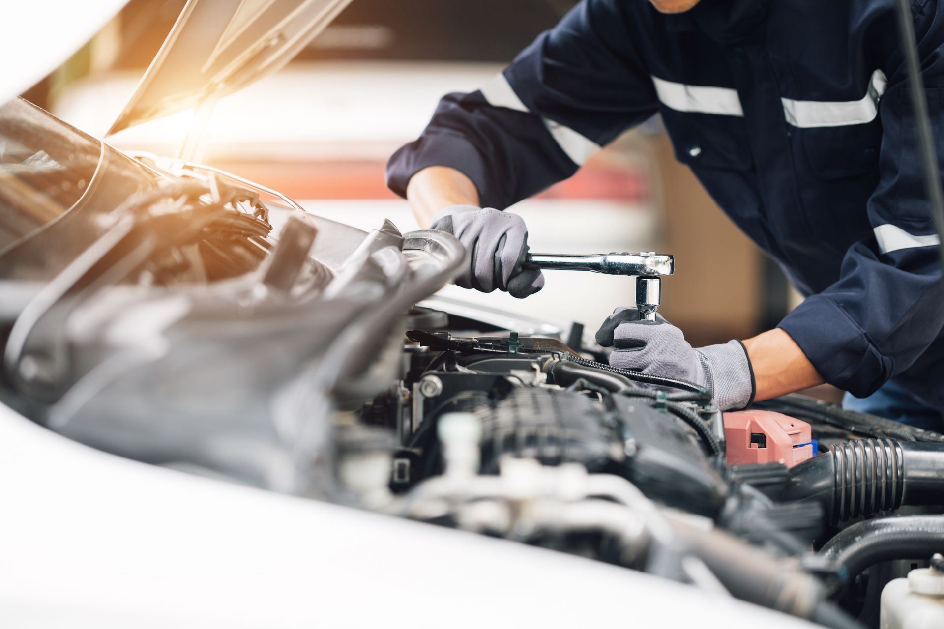 Mechanic in dark uniform working under a car hood in a garage, using tools to repair the engine