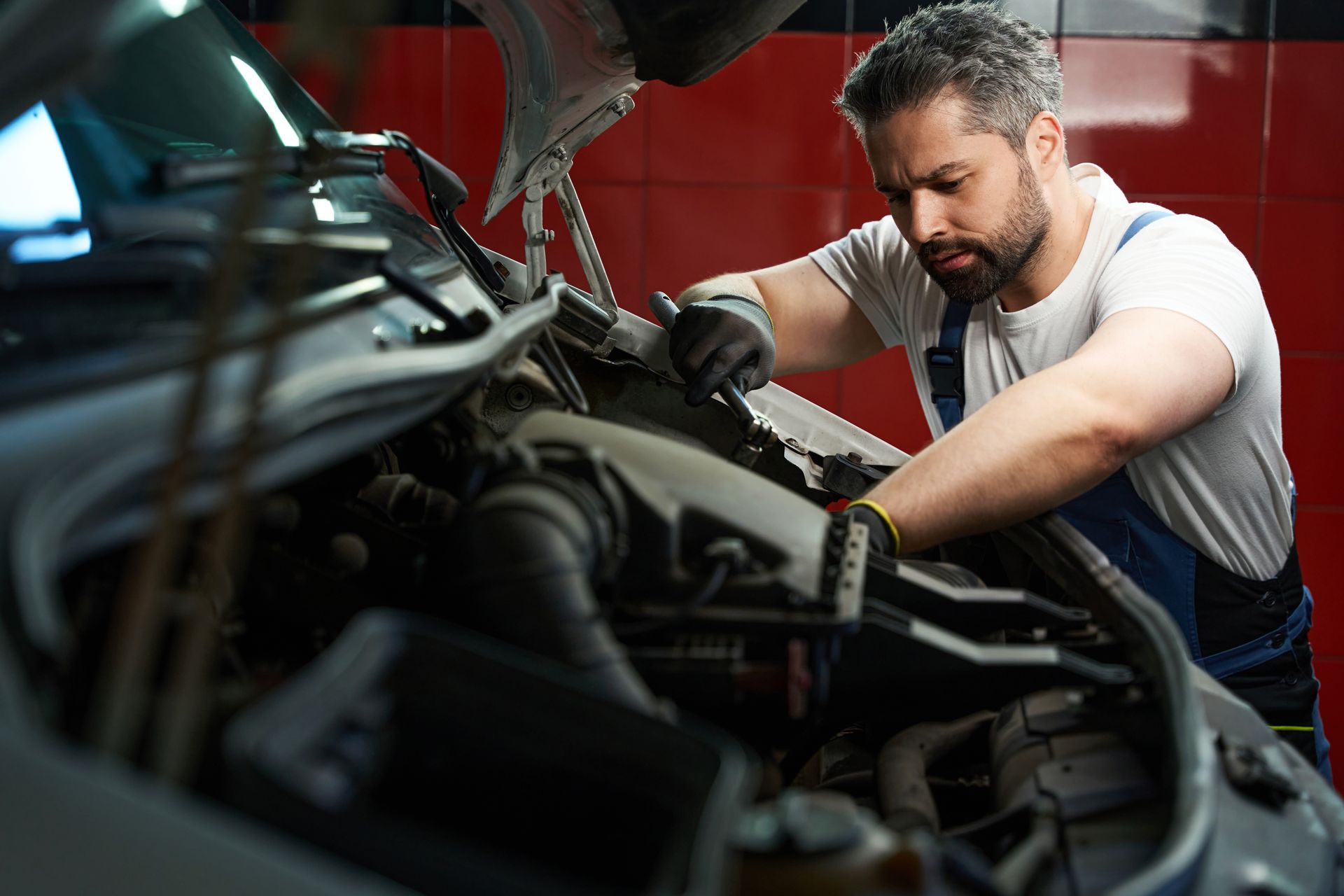 A focused mechanic is performing automotive repair on his customer's vehicle with a wrench.