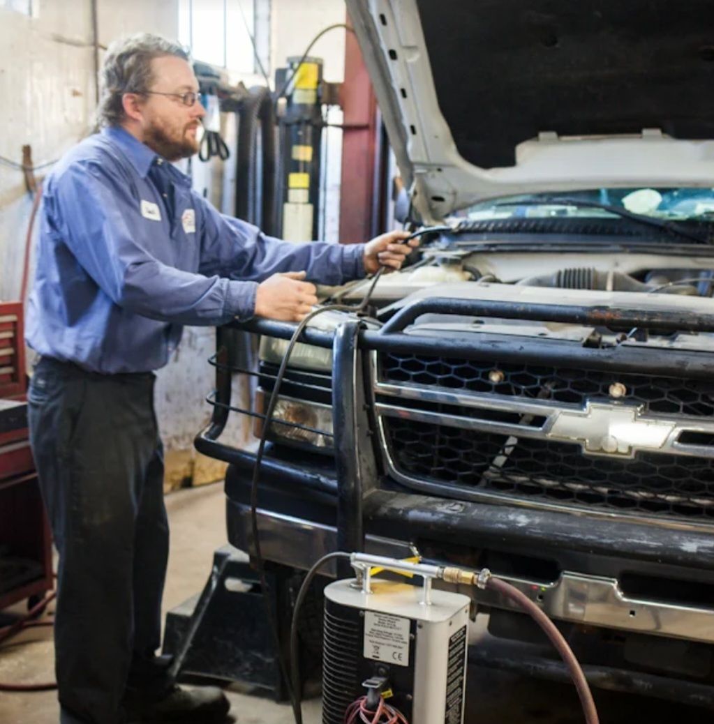 A technician in a blue uniform inspecting an open Chevrolet truck engine in a workshop.