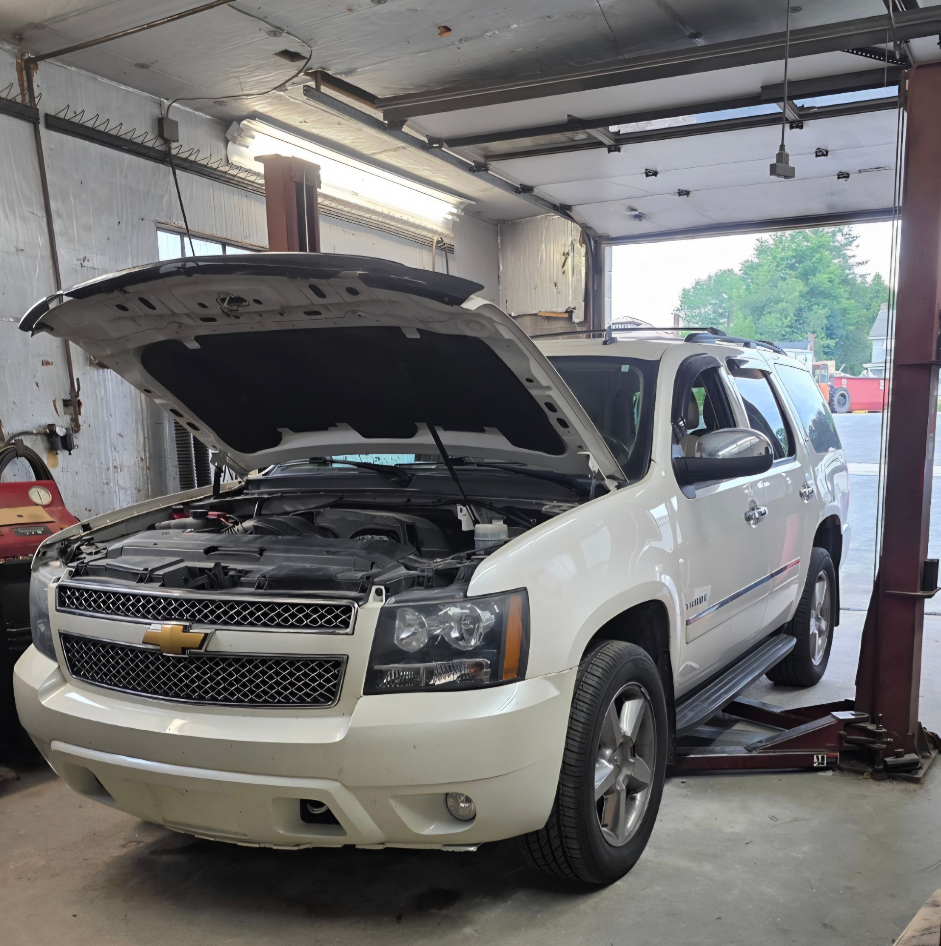 A white Chevrolet SUV parked inside an auto repair shop with its hood open for maintenance.