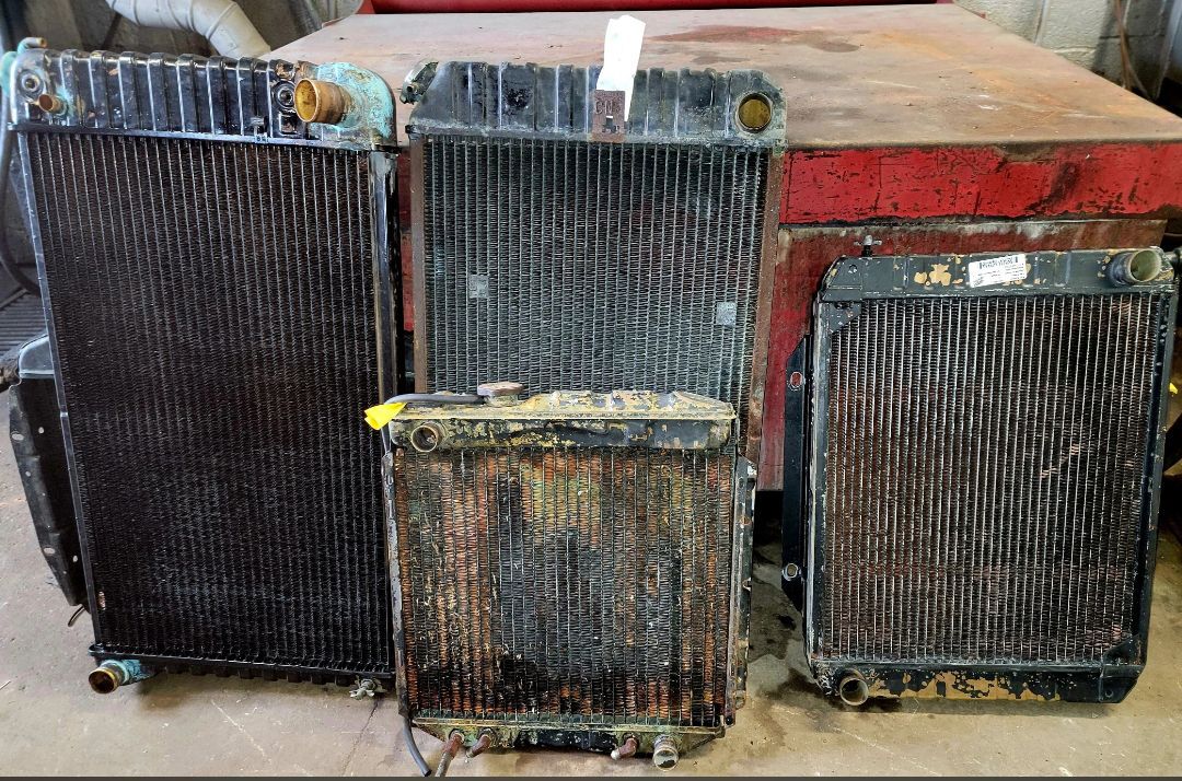Four old, weathered vehicle radiators of varying sizes resting on a wooden surface.
