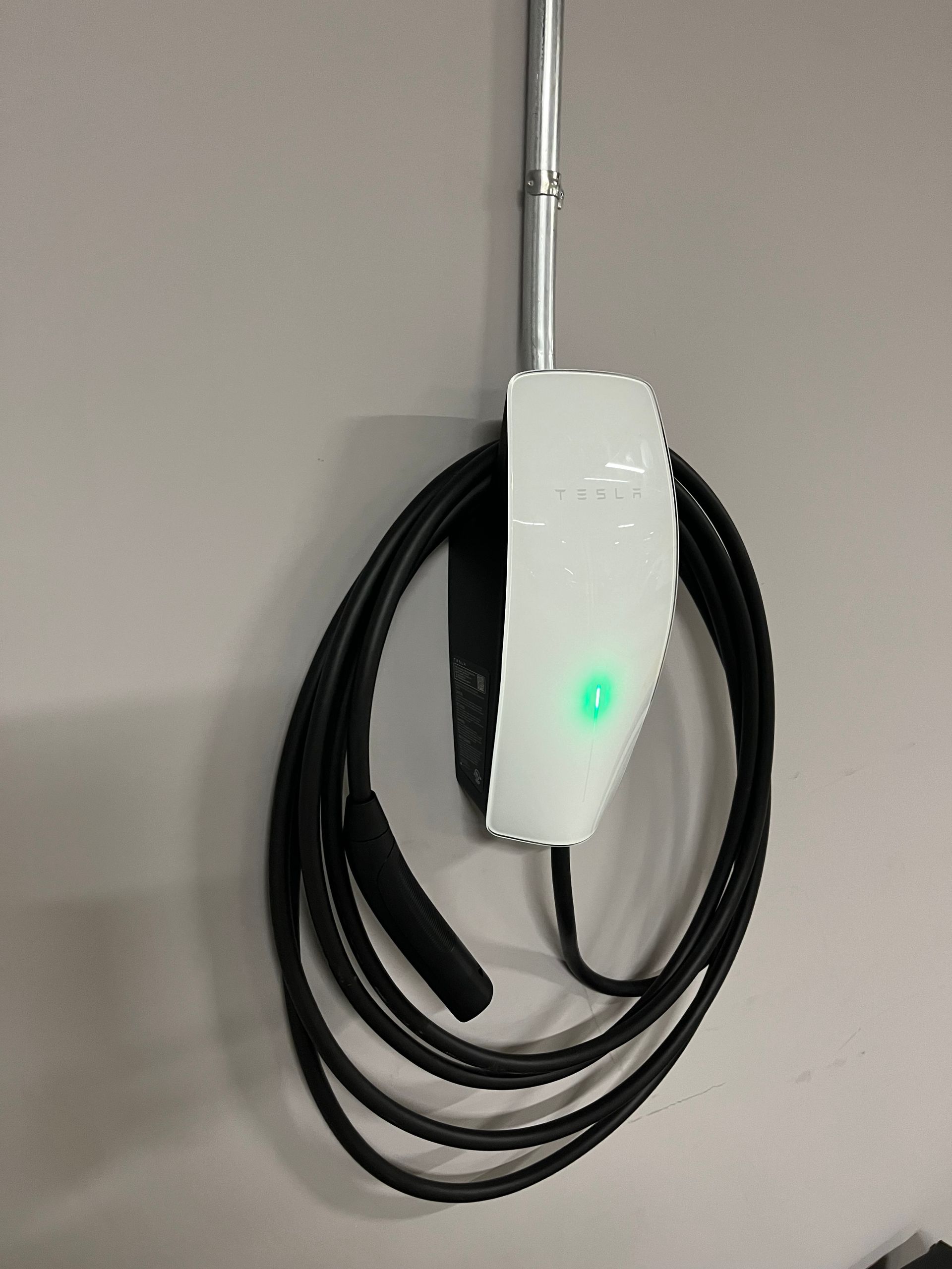 Un chargeur Tesla est accroché à un mur avec un câble noir attaché.