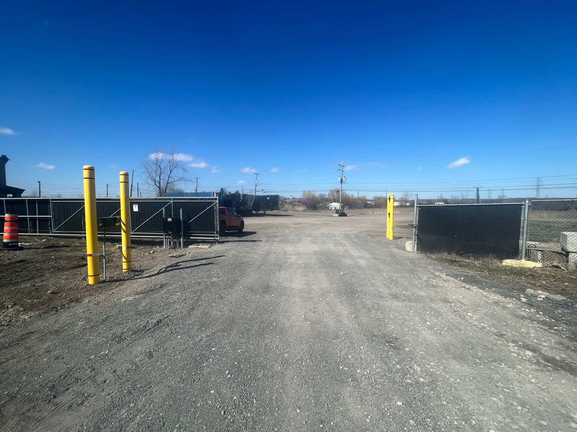 Un chemin de gravier menant à une zone clôturée avec un ciel bleu en arrière-plan.