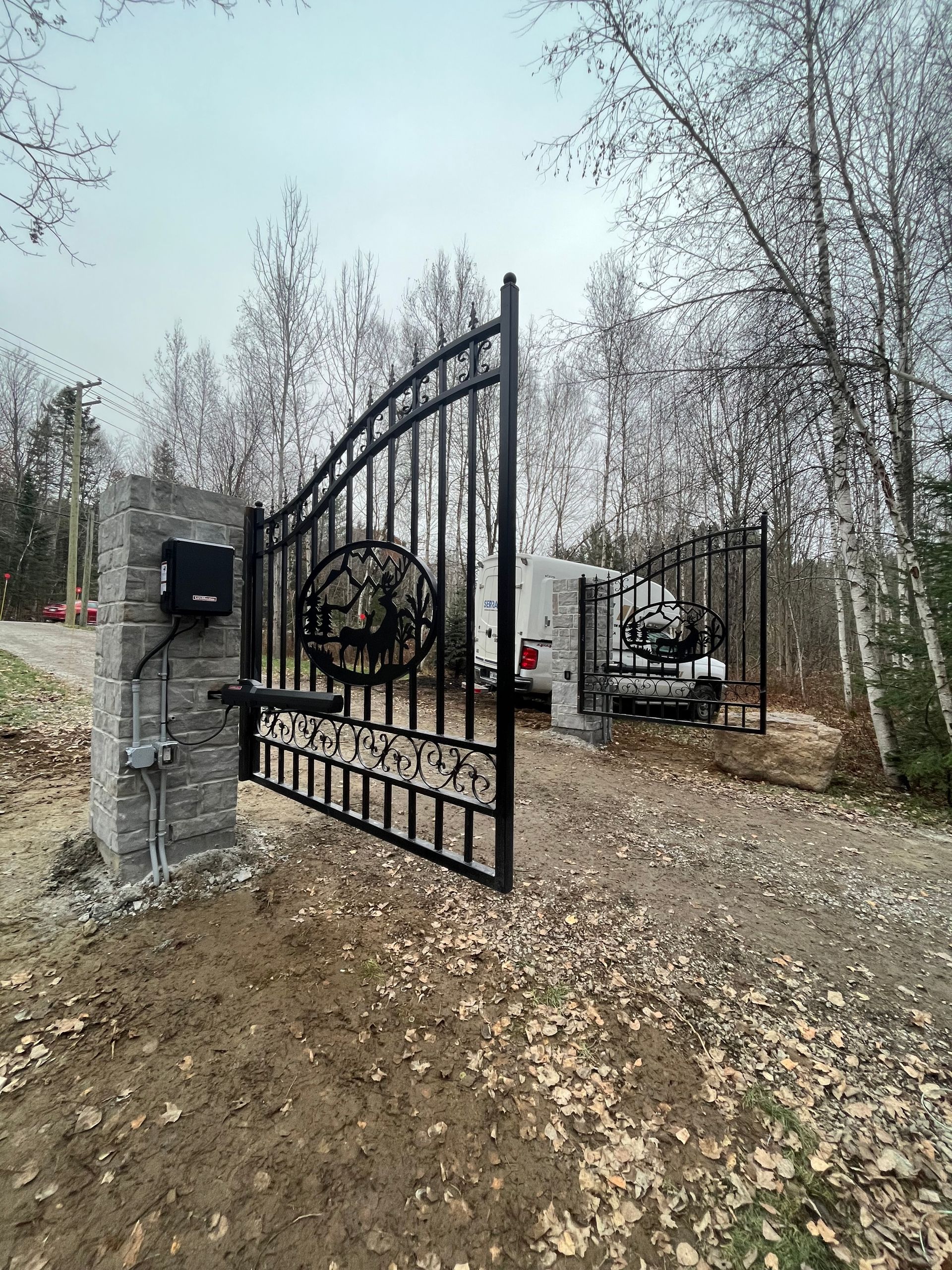 Un portail en fer forgé s'ouvre sur une allée entourée d'arbres.