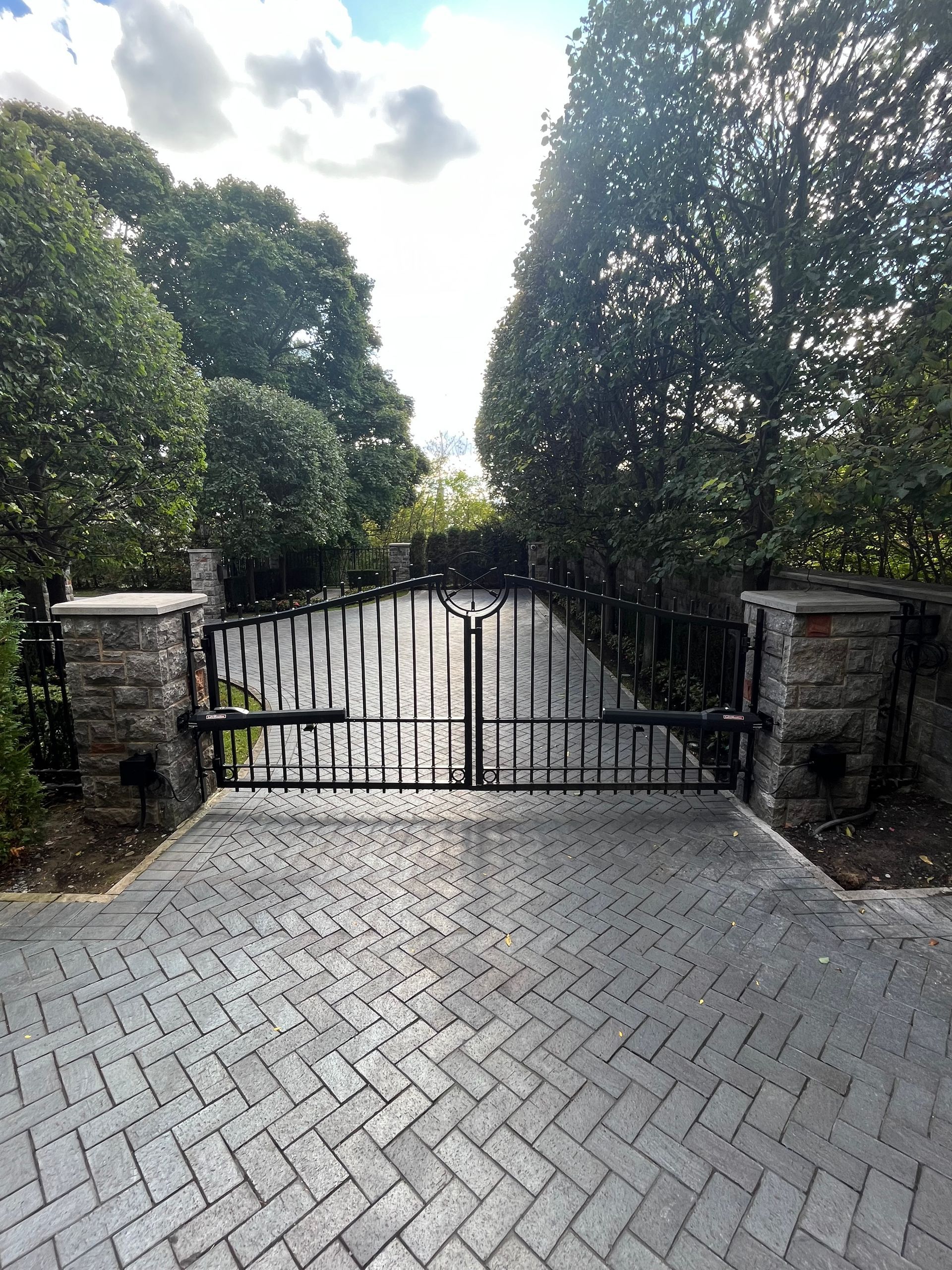 Une allée en briques avec un portail en fer forgé et des arbres en arrière-plan.