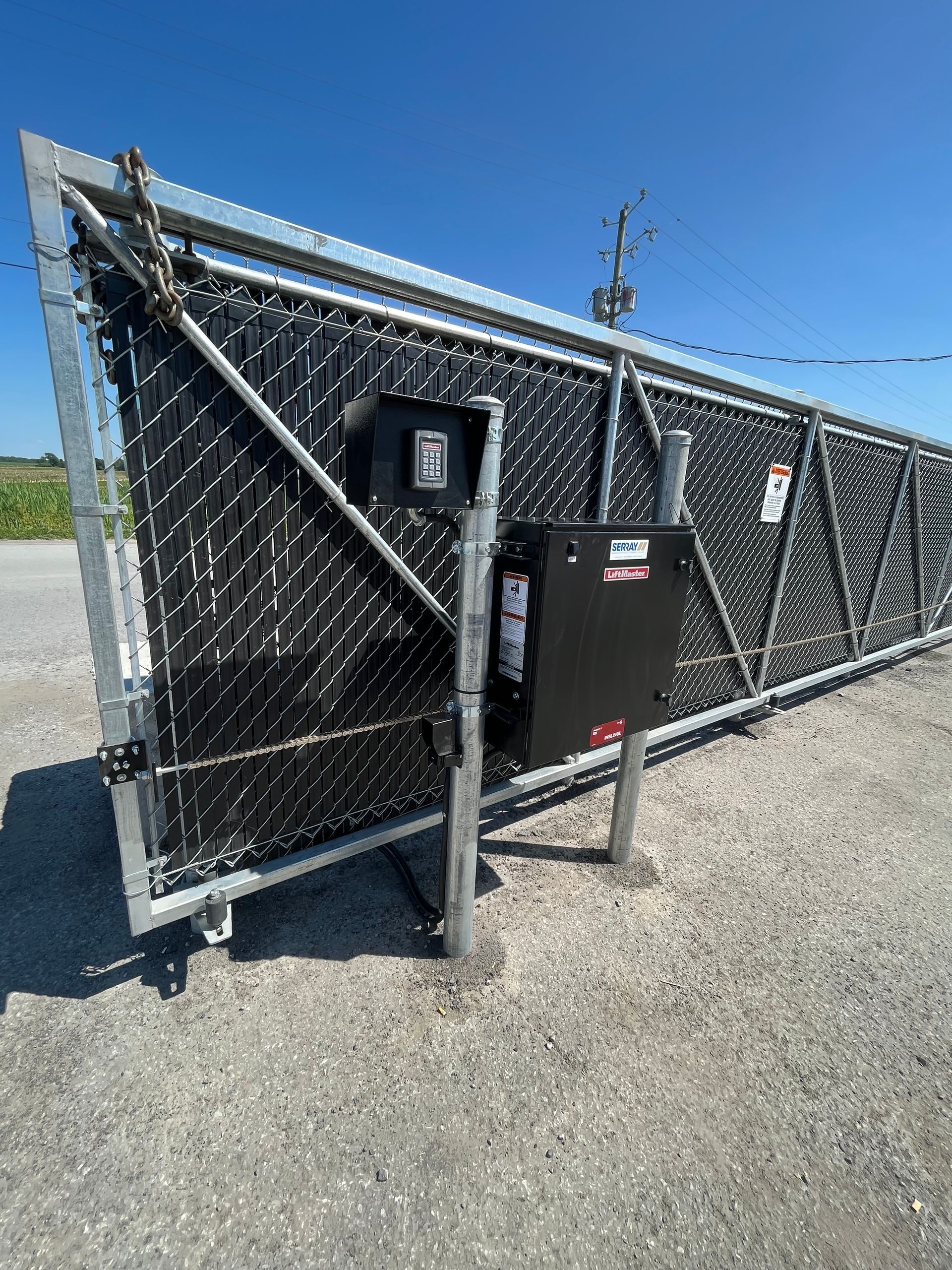 Une clôture à mailles losangées est posée sur une route de gravier.