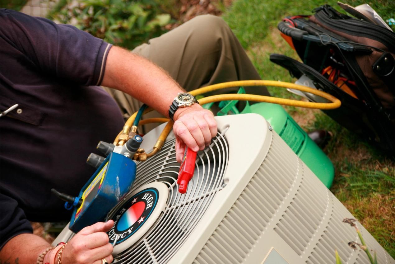 Technician checking an outdoor air conditioner with a red gauge and hoses attached