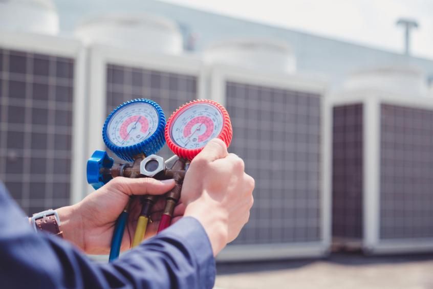 Technician holding HVAC gauges in front of outdoor air conditioning units
