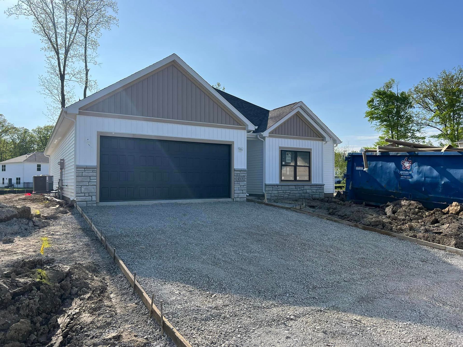 A house is being built with a large garage and a gravel driveway.