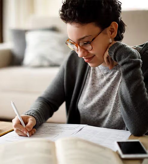A woman is sitting at a table writing on a piece of paper.