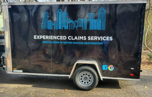 A black trailer for experienced claims services is parked on the side of the road.