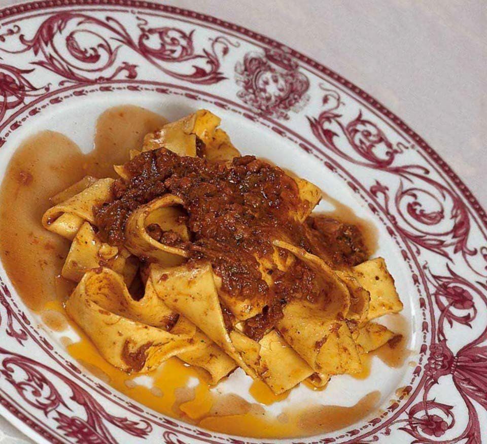 Pasta al ragù su un piatto bianco con bordo decorato con fiori rossi.