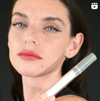 Una mujer con pecas sostiene un brillo de labios en la mano