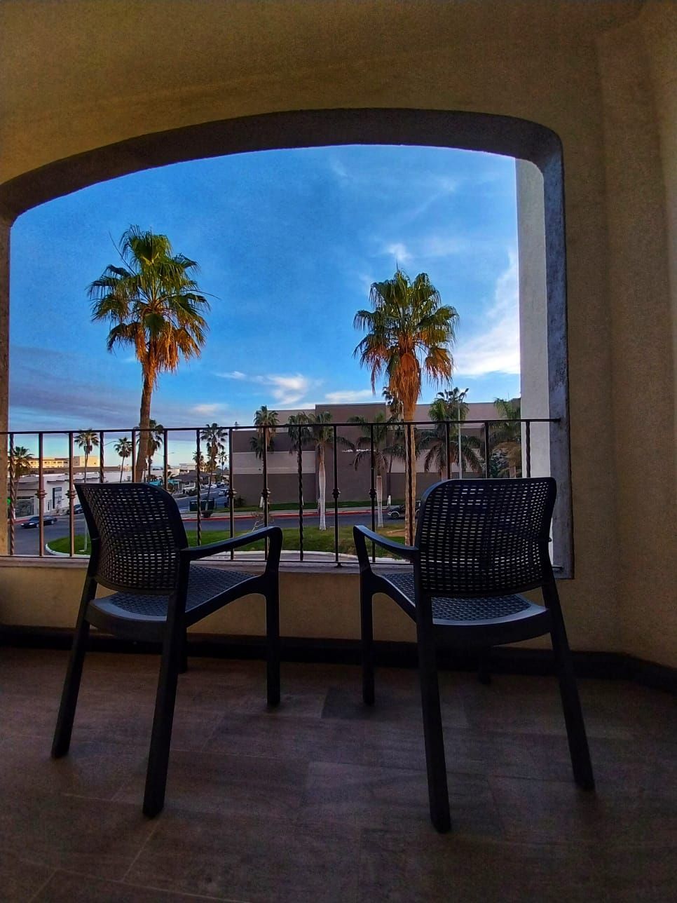 Two chairs on a balcony with palm trees in the background