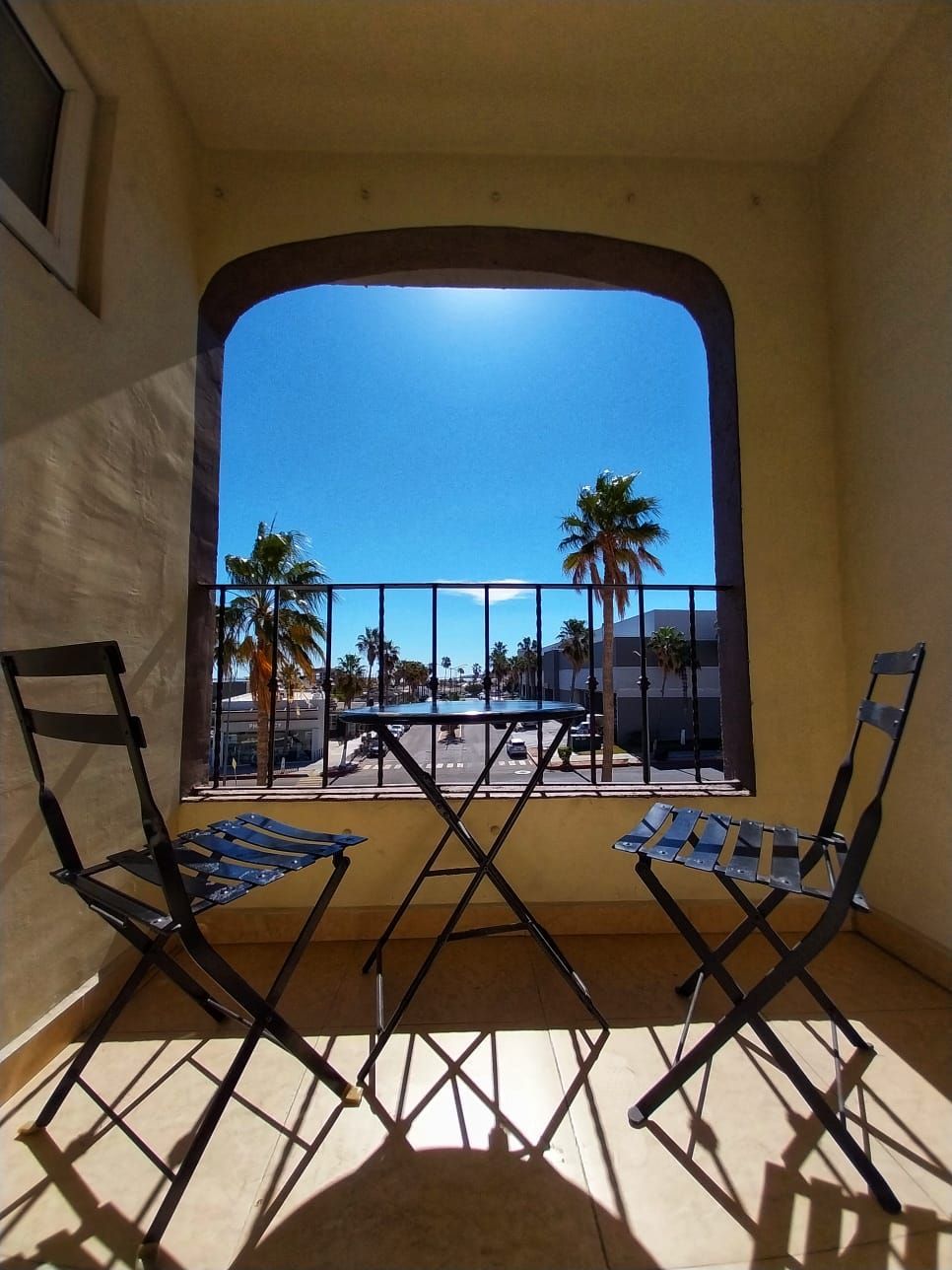 A balcony with two chairs and a table with palm trees in the background