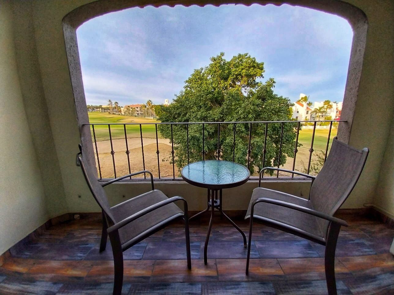A balcony with two chairs and a table with a view of a golf course.