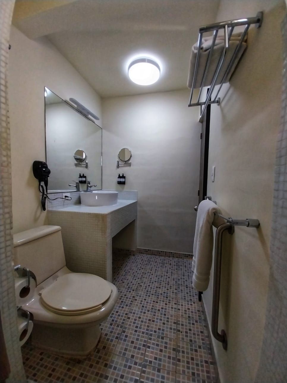 A bathroom with a toilet , sink , mirror and towel rack.