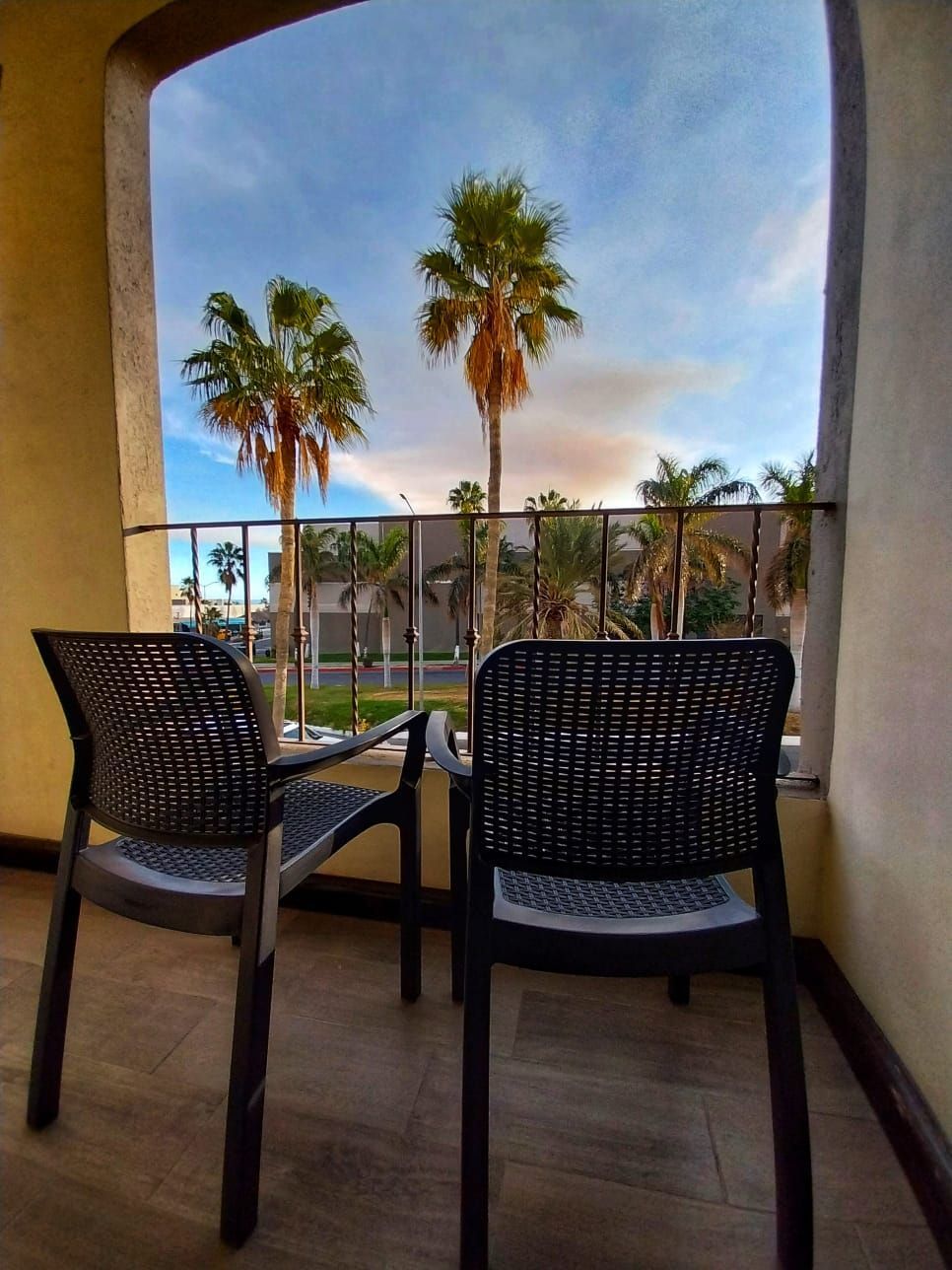 A balcony with two chairs and a table with palm trees in the background