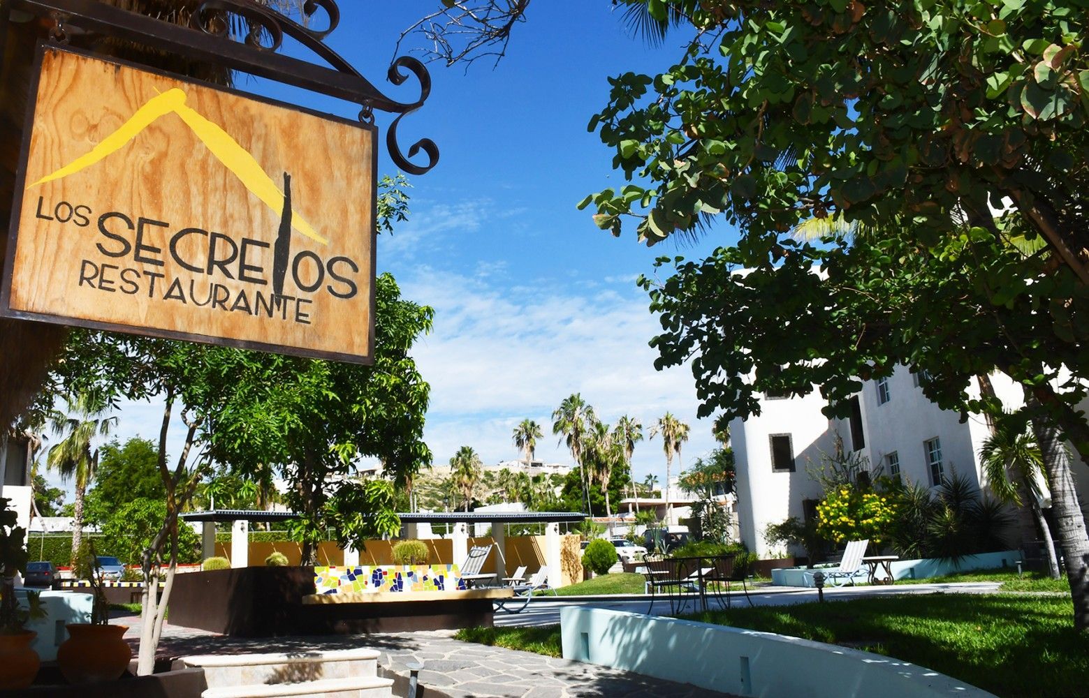 A sign for los secretos restaurant hangs from a tree
